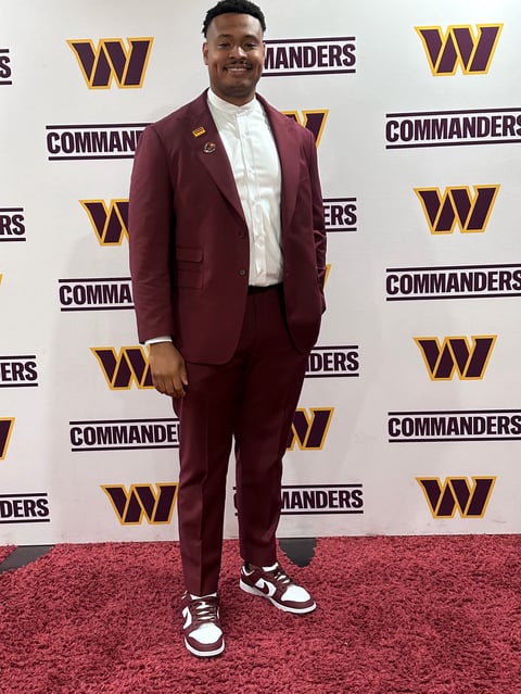 Man in maroon suit and white shirt smiling at Washington Commanders event on red carpet