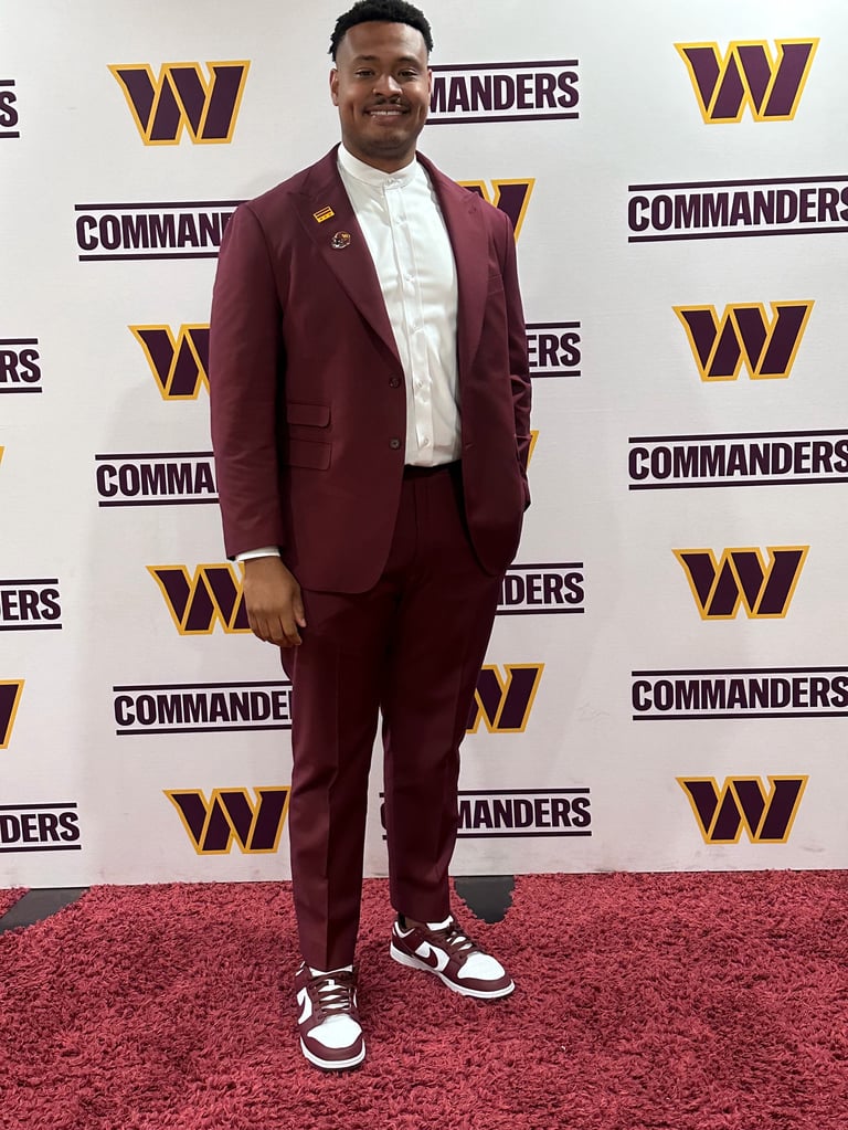Man in maroon suit and white shirt smiling at Washington Commanders event on red carpet
