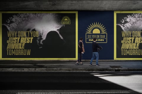 Street billboard advertisement with motivational messaging and concert tour promotion, person standing in front viewing the display