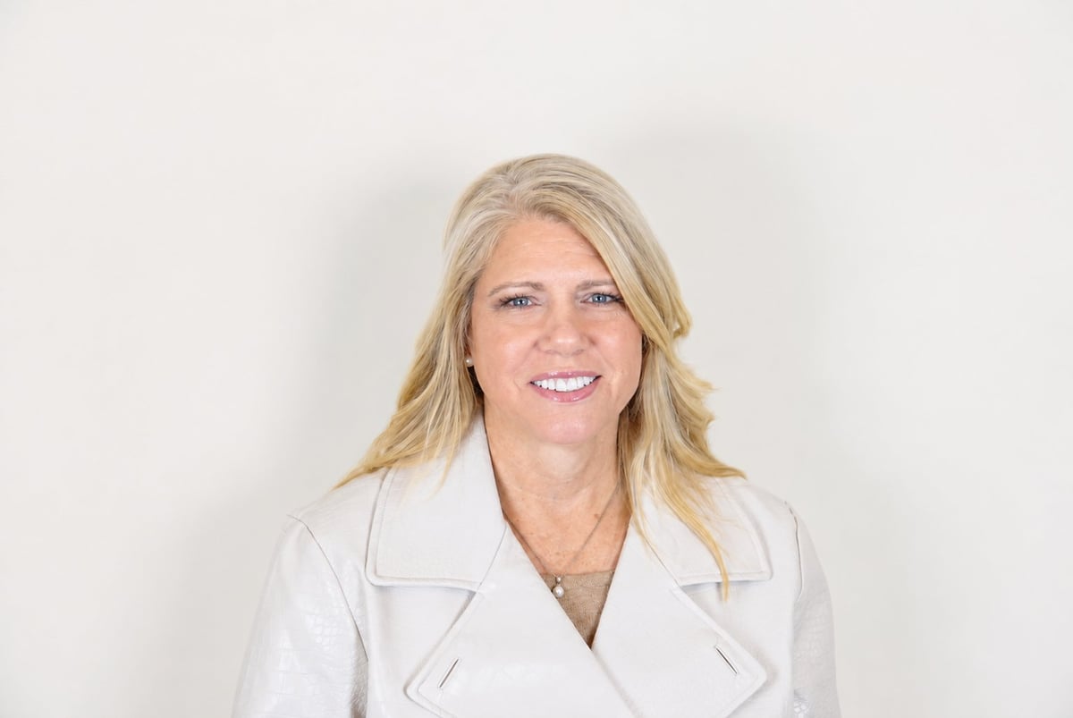 Woman with blonde shoulder-length hair wearing a white blazer, smiling at the camera against a white background
