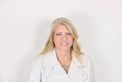 Woman with blonde shoulder-length hair wearing a white blazer, smiling at the camera against a white background