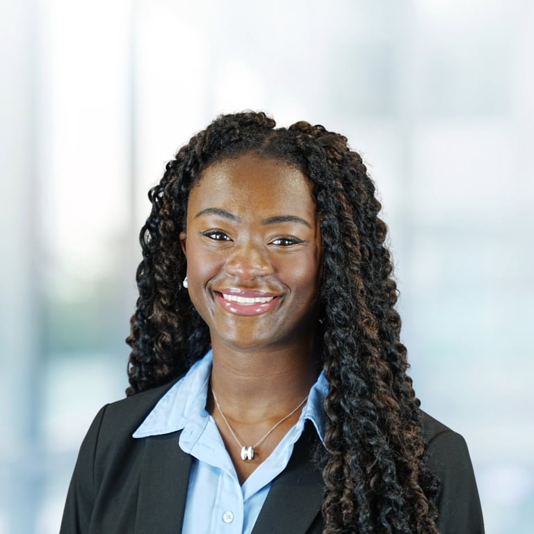 Professional headshot of a smiling woman with long braided hair wearing a black blazer and light blue blouse