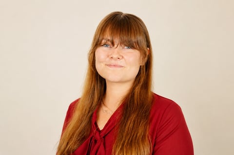Woman with long reddish-brown hair and bangs wearing a red top against a neutral background