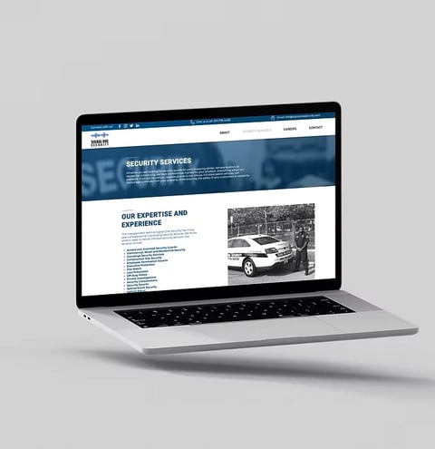 Silver laptop displaying a security services website with a blue header banner and content sections