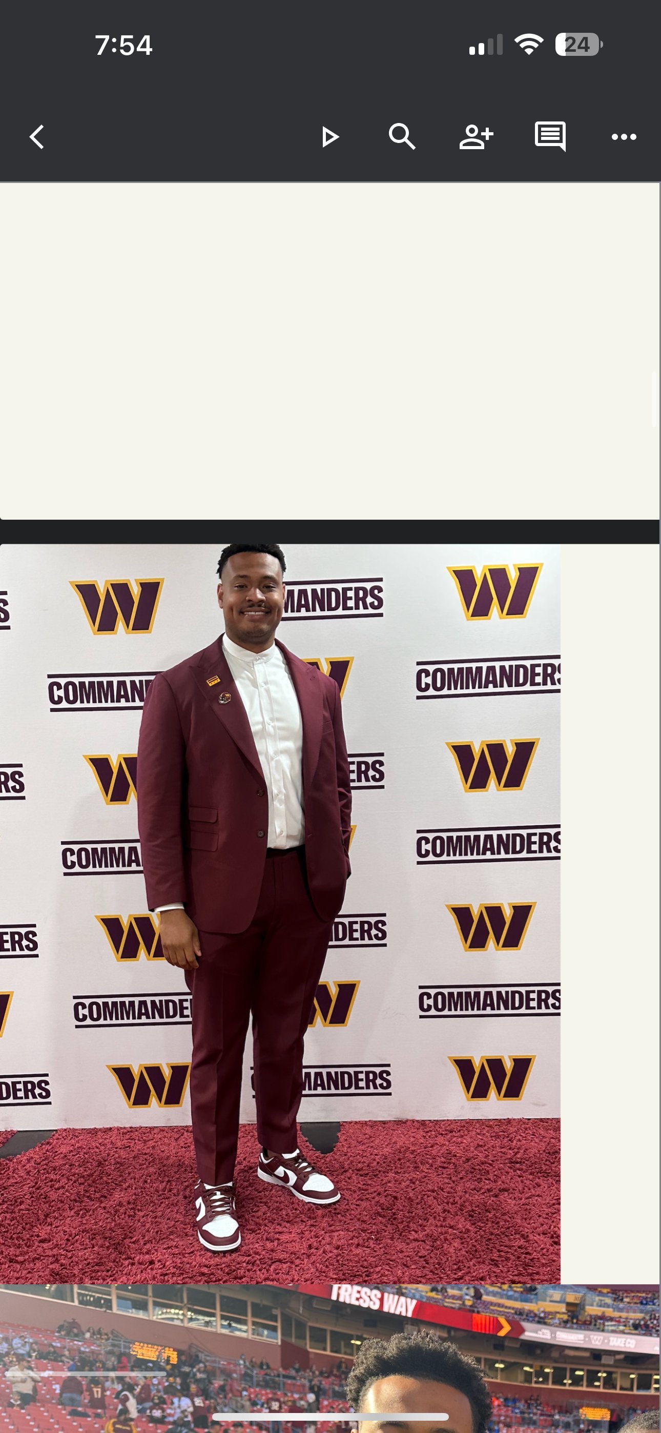 Man in maroon suit and sneakers posing at Washington Commanders branded media backdrop