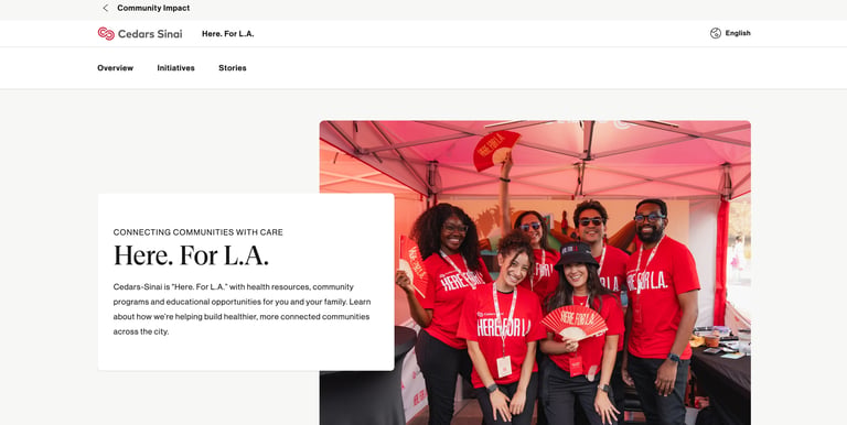 Group of people wearing red Cedars-Sinai shirts smiling at a community event under a pink tent