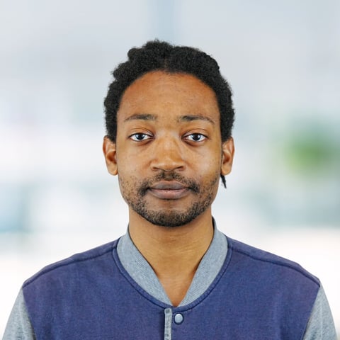 Portrait of a man with dark hair and facial hair wearing a navy and gray cardigan against a blurred background