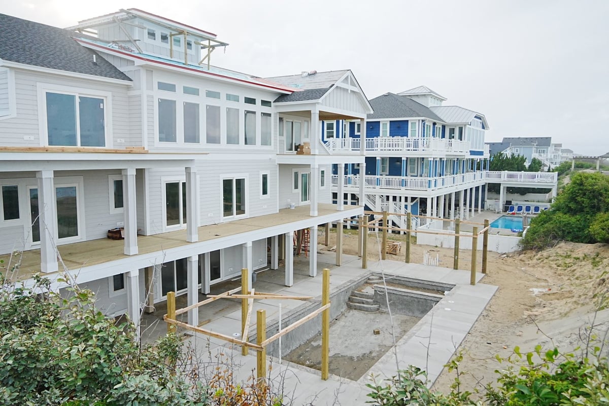 Beachfront residential neighborhood with modern white multi-story homes built on stilts overlooking sandy dunes and ocean