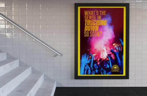 Vibrant concert poster with yellow frame on white tiled wall next to modern staircase, featuring colorful text and crowd silhouettes