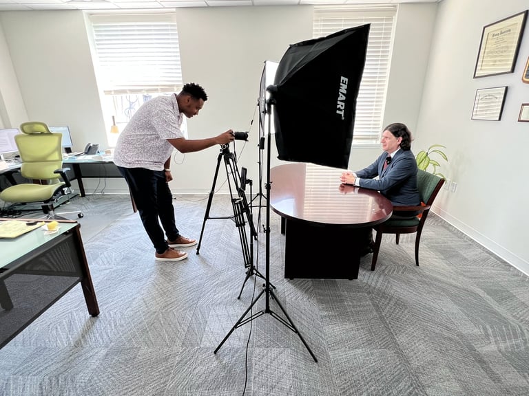 Professional video interview setup with cameraman operating tripod-mounted camera and woman seated at table under studio lighting