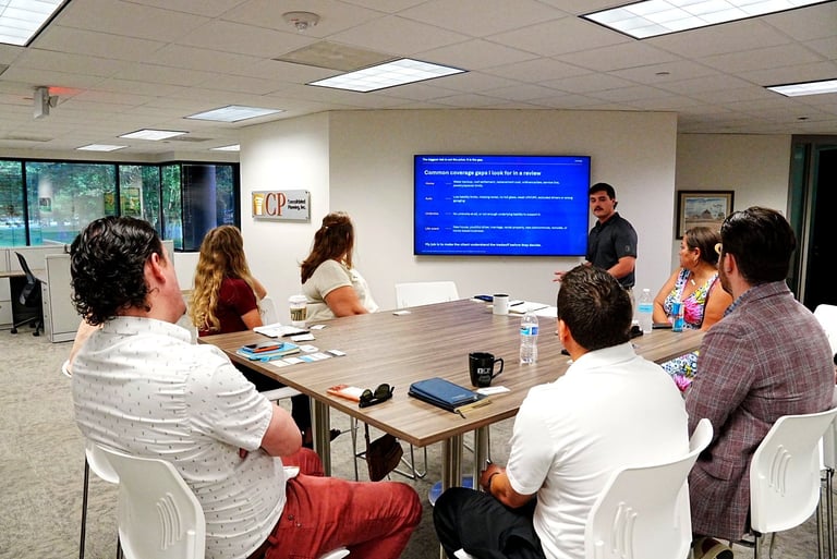 Group of people sitting around a table in a conference room with a presenter showing content on a blue screen display