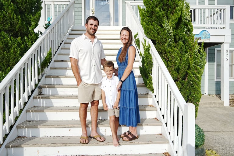 Family of three standing on white wooden beach house stairs in casual summer clothing
