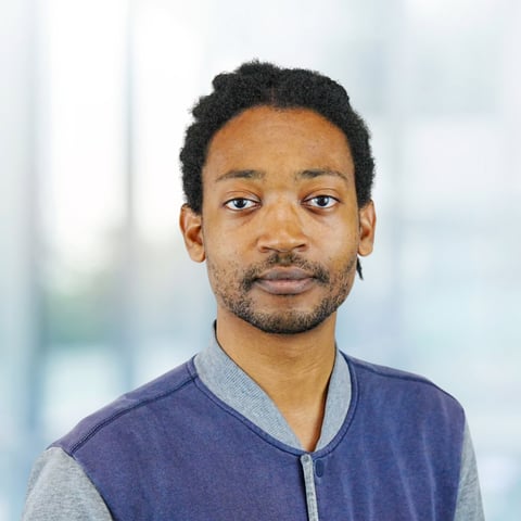 Portrait of a man wearing a navy and gray color-blocked sweater against a blurred light background