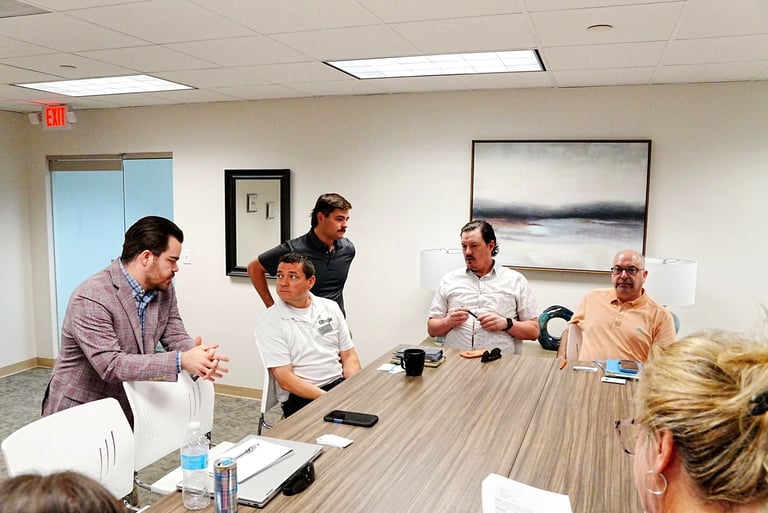 Five people gathered around a wooden conference table in an office meeting room, engaged in discussion