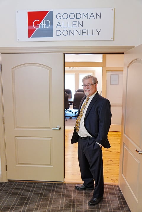 Man in dark suit and patterned tie standing in doorway of Goodman Allen Donnelly office entrance
