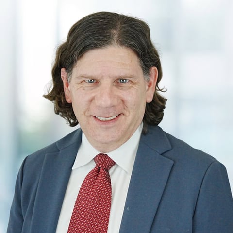 Professional portrait of a man with dark shoulder-length hair wearing a dark blue blazer and red tie