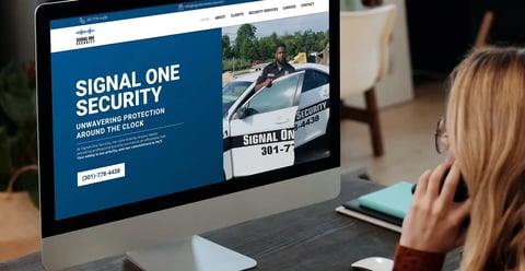 Woman viewing Signal One Security website on desktop monitor displaying home security services and patrol vehicle