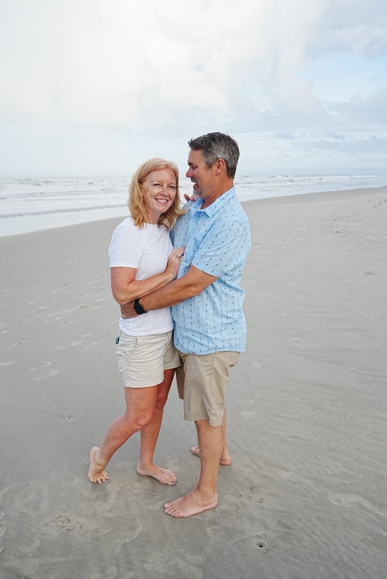 Middle-aged couple embracing on a sandy beach with ocean waves in the background on an overcast day