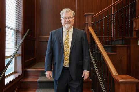 Older man in blue blazer and patterned tie standing on wooden staircase in elegant interior