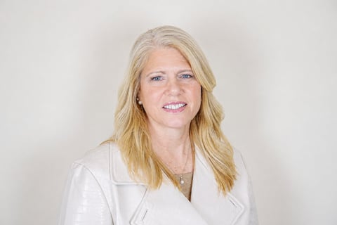 Professional headshot of a woman with blonde shoulder-length hair wearing a white blazer against a neutral background