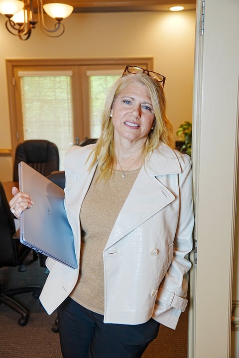 Woman in white blazer holding tablet in office, wearing glasses on head, smiling at camera