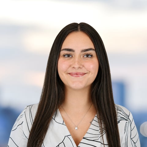 Portrait of a young woman with long dark hair wearing a striped shirt, smiling at the camera with a blurred cityscape background