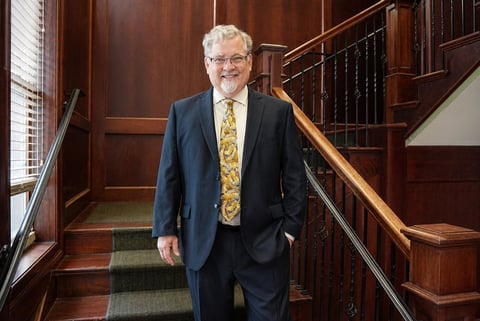 Senior man in dark suit and patterned tie standing on wooden staircase in professional building interior