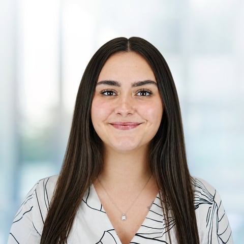 Professional headshot of a woman with long black hair wearing a striped white shirt, smiling at camera against a blurred office background