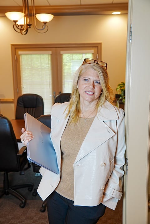 Woman smiling in office holding a tablet, wearing a cream blazer and sunglasses pushed up on her head
