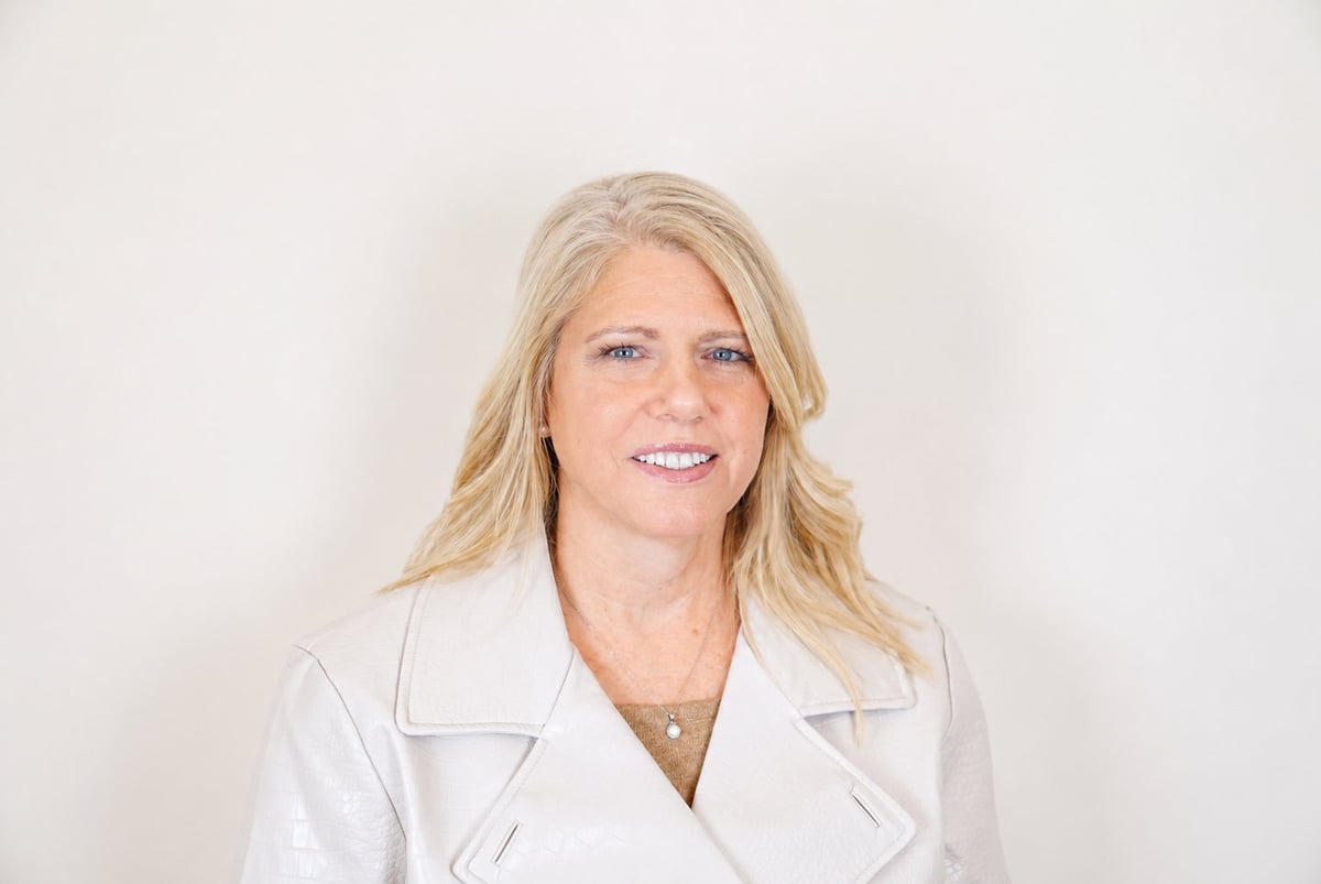 Professional portrait of a woman with blonde wavy hair wearing a white blazer against a neutral background