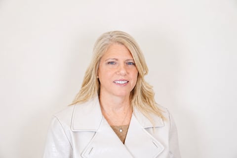 Professional portrait of a woman with blonde wavy hair wearing a white blazer against a neutral background
